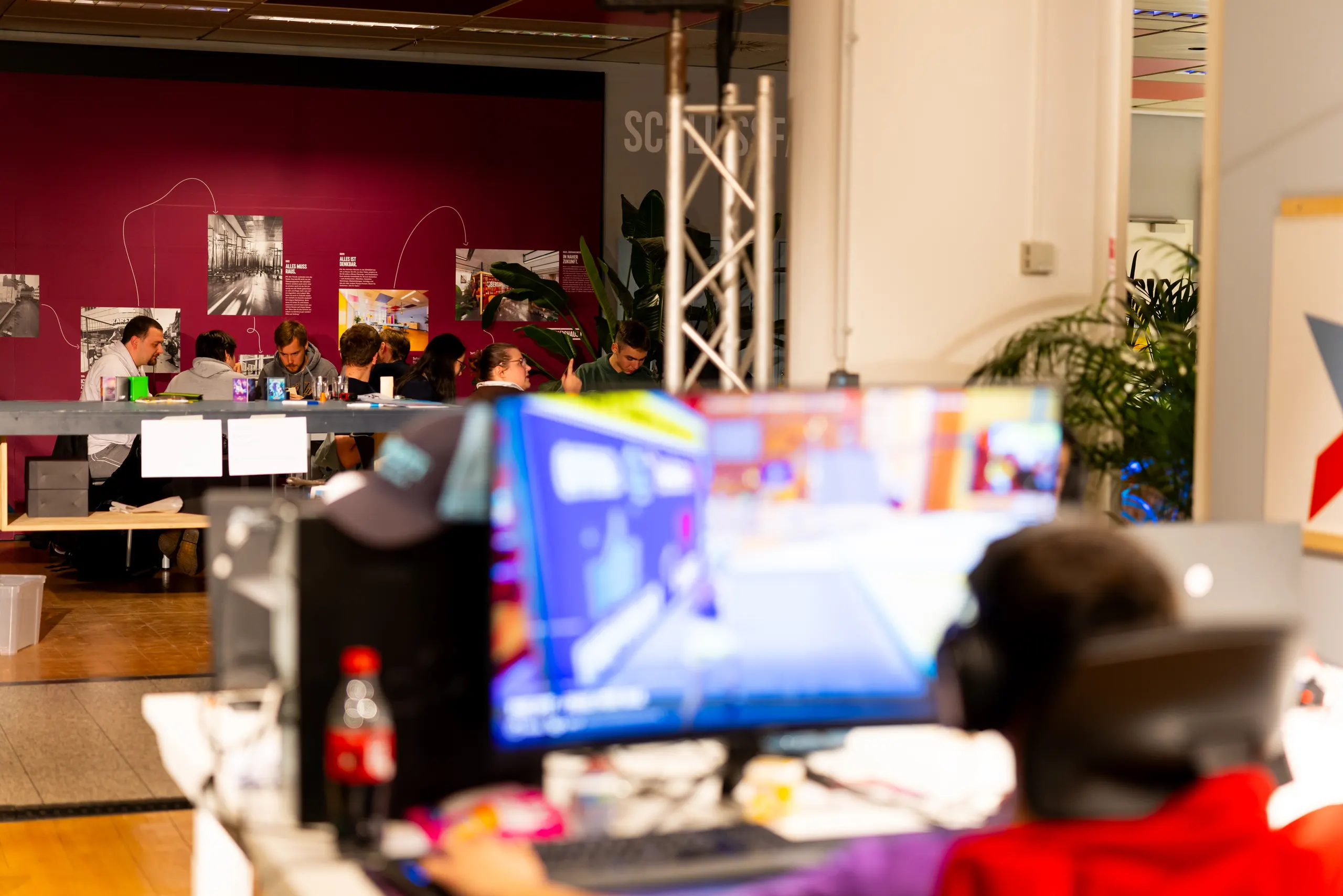 Menschen an einem gemeinsamen Tisch im Ausstellungsraum des Hansemuseums, im Vordergrund ein Gaming-Setup mit Kopfhörern