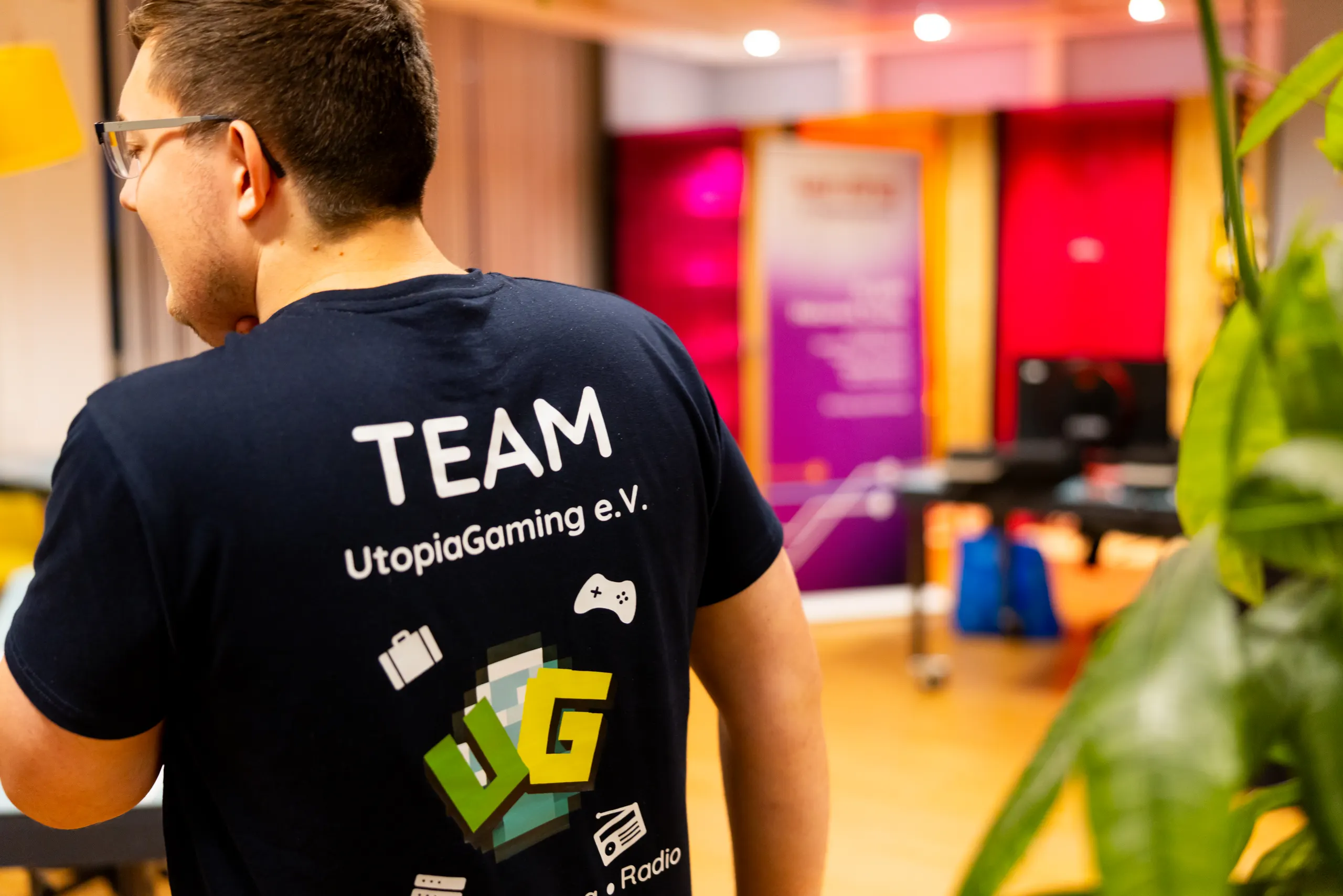 Teammitglied von hinten im Vereinsshirt des UtopiaGaming e.V., auf dem neben dem UG-Logo ein Radio-Symbol zu sehen ist